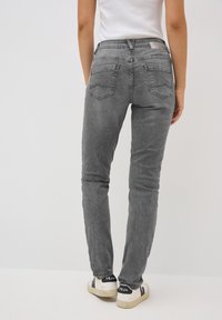 Jeans in denim grigio slim-fit con una texture sbiadita, design a cinque tasche e cuciture riconoscibili sulla tasca posteriore. Indossati con sneakers casual.