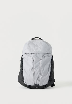 Lichtgrijze en zwarte North Face Surge rugzak met voorvakken en bovenste handvat op een witte achtergrond.