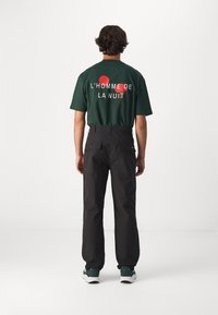 T-shirt en coton vert avec le texte graphique rouge "L'HOMME DE LA NUIT" au dos. Accompagné d'un pantalon cargo noir avec deux poches arrière.
