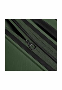 Dettaglio della cerniera di una valigia verde con un tessuto texturizzato. Presenta una cerniera nera e bordature. La vista ravvicinata enfatizza il materiale e la costruzione.