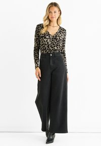 Top avvolgente a maniche lunghe con stampa leopardata, pantaloni in denim neri a vita alta e gamba larga, e stivaletti neri con punta. Tessuto morbido e design aderente.
