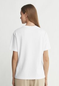 Hvid kortærmet t-shirt med en afslappet pasform, rund halsudskæring og blød tekstur, parret med lysebeige bukser.