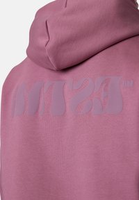 Pink hoodie featuring a large, tonal "MTS" logo on the back, made from soft fabric with a smooth texture. Attached hood detail visible.