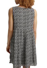 Femme aux cheveux bouclés portant une robe noire sans manches avec un motif floral blanc, vue de dos