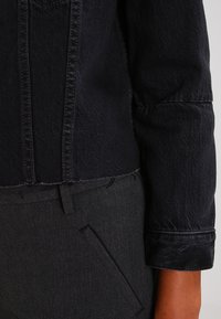 Mörk denimjacka med en kortad design och strukturerade axlar. Har synlig sömnad och en jämn tygtextur. Matchas med skräddarsydda grå byxor.