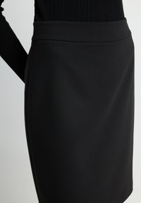 Gonna a matita nera realizzata in tessuto liscio con una vita alta e una forma aderente, che mette in mostra un design pulito e minimalista.