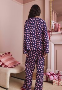Tumesinine pidžaamakomplekt roosa tähekese mustriga, millel on pikad varrukad ja laiad püksid, kombineeritud pehmete sussidega. Mugav kangastekstuuri.