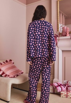 Navy pajama set with pink star pattern, featuring long sleeves and loose-fitting pants, paired with fuzzy slippers. Cozy fabric texture.