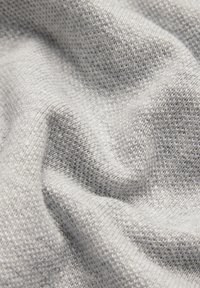 Jasnoszara dzianina o miękkiej, teksturowanej powierzchni i małych, równych ściegach, prezentująca delikatny układ i subtelną głębię.