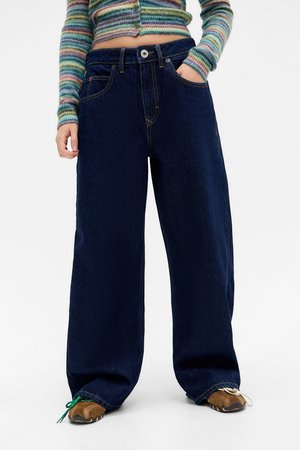 Bredde ben av mørk denim med høy midje, med sidelommer og synlig søm. Kombinert med brune sneakers.