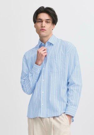 Camisa de botón azul claro con rayas verticales blancas, de mangas largas, con un bolsillo en el pecho y un corte relajado, fabricada con una tela suave.