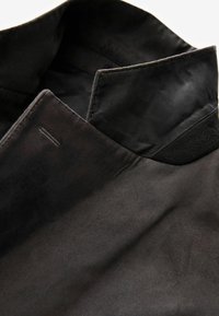 Schwarzer Stoffkragen mit schlankem Design; glatte, matte Textur; dezente Nahtdetails entlang der Kante; strukturierte Form.