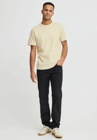 Beige bomulds T-shirt parret med sorte jeans og hvide sneakers. T-shirten har rund hals og korte ærmer, med et minimalt design.
