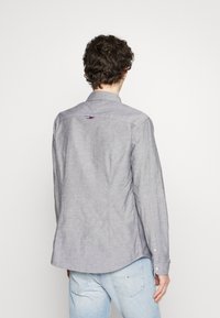 Gray button-up shirt with long sleeves, made of a soft fabric. Features a curved hem and small logo detail on the upper back.