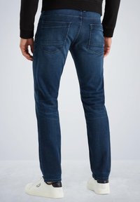 Vaqueros de mezclilla azul oscuro con corte ajustado, con bolsillos traseros y detalles de costura sutiles. Combinados con zapatillas blancas y negras.