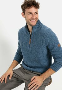 Blauer Strickpullover mit hohem Kragen, Reißverschluss, gerippten Bündchen und Lederakzenten an den Ärmeln. Wärmender, strukturierter Stoff mit feinen Sprenkeln.