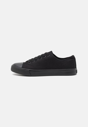 Black canvas sneakers with a rounded toe, rubber cap, and flat sole. Features six eyelets and contrasting stitching. Simplistic design.