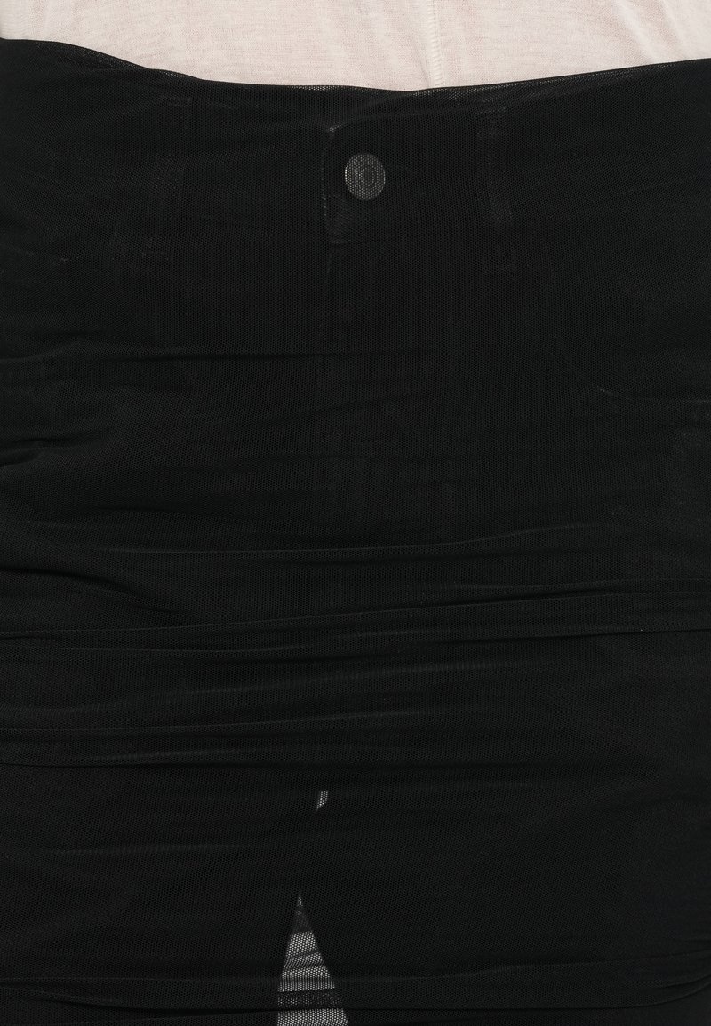 Schwarzer, hoch taillierter, geraffter Rock mit vorderem Knopf und Schlitz, getragen vor einem hellbeigen Stoffhintergrund.