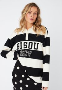 Long-sleeve polo shirt with black and white horizontal stripes. Features a collar, button closure, and "BISOU 1975" print. Soft fabric.
