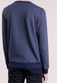 Tmavě modrá texturovaná mikina s žebrovaným kulatým výstřihem, kontrastními tmavými manžetami a lemem. Materiál má jemný vzor, který dodává hloubku.