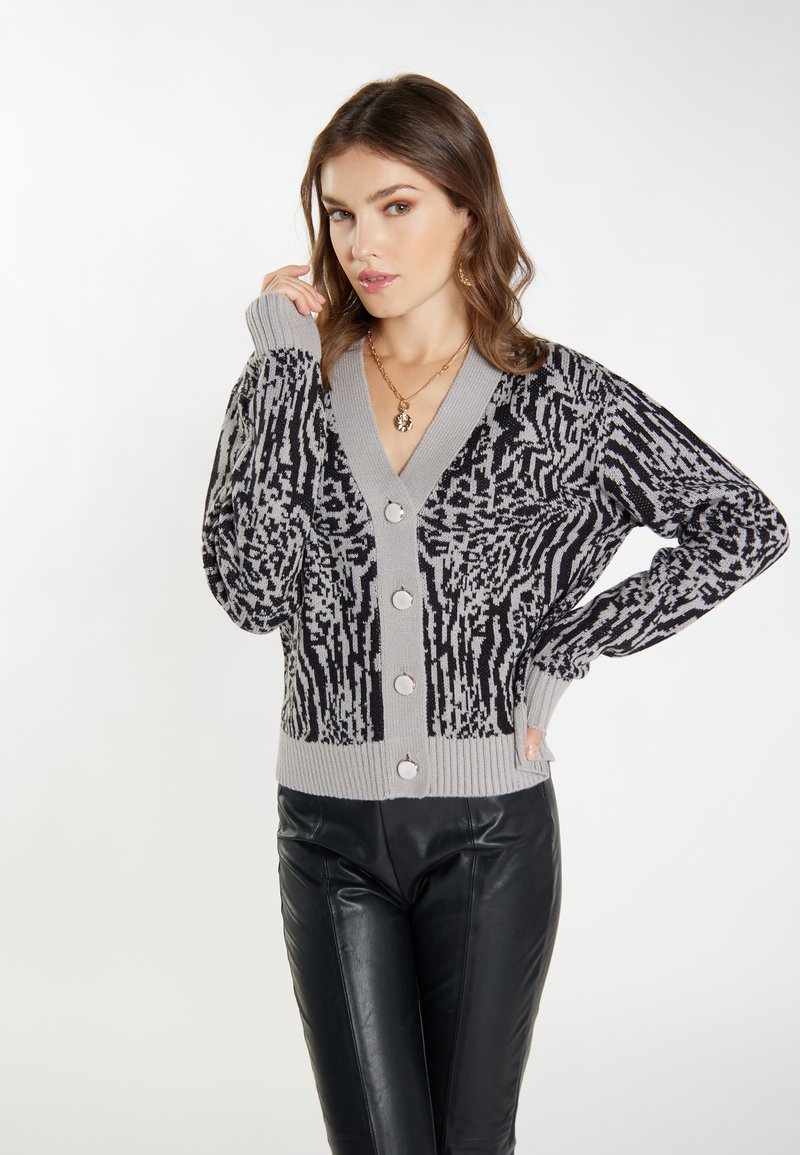 Grå og sort mønstret cardigan med V-hals, lange ærmer og store knapper, featuring en ribbet søm og tekstureret stof.
