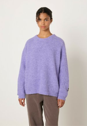 Paarse, oversized gebreide trui met een textuurpatroon en een ronde halslijn. Zacht materiaal met verlaagde schouders, gecombineerd met een paarse broek.