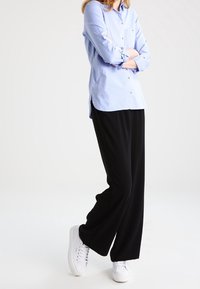 Ljusblå skjorta med knäppning och uppvikt ärm; svarta, vida byxor; vita sneakers; minimalistisk design, släta texturer genomgående.