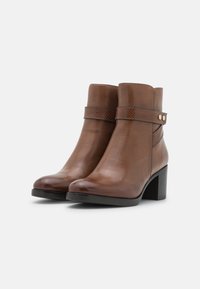 Bottes en cuir marron jusqu'à la cheville avec une bande texturée et des accents dorés. Dotées d'un bout rond et d'un talon bloc. Finition lisse avec un design élégant.