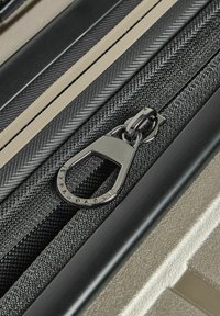 Tirante della cerniera di valigia espandibile in metallo argentato, con una fascia in nylon nero testurizzato su uno sfondo elegante e metallico oro.