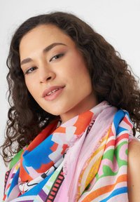 Écharpe multicolore présentant des motifs audacieux en rouge, bleu, vert et rose avec un bord frangé ; fabriquée en tissu léger.