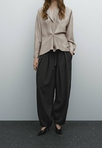 Blazer beige texturé avec un col pointu, associé à un pantalon noir ample et des talons noirs. Les deux vêtements présentent des éléments de design minimalistes.