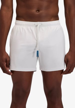 Torace e gambe maschili che indossano pantaloncini da bagno bianchi con fascia elastica in vita e coulisse con estremità blu su sfondo bianco uniforme.