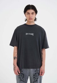 Camiseta negra de gran tamaño hecha de algodón, con un logo blanco de "ED HARDY". Destacan sus mangas cortas y un diseño de cuello redondo.