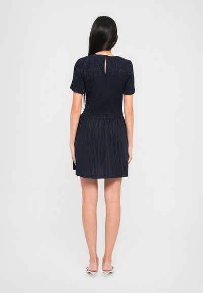 Tengerészkék ruha rövid ujjakkal, redőzött tetejű, harangszoknyás és hátul kulcslyuk részletekkel. Simább textúra, térd mögé érő, függőleges csíkokkal.