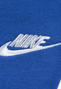 Kék szövet sima felülettel, fehér hímzett Nike logóval és alatta egy swoosh mintával.