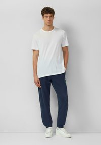 Biała bawełniana koszulka w połączeniu z granatowymi spodniami dresowymi ozdobionymi haftowanym zielono-czerwonym wzorem, uzupełniona białymi trampkami.