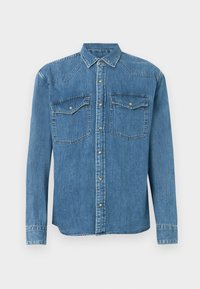 Chemise en denim bleu clair, avec des manches longues, un col pointu, deux poches avant avec rabat, et des boutons pression en argent.