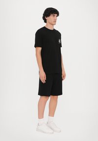 Svart bomull T-skjorte med korte ermer, med en liten logo på brystet, kombinert med svarte shorts og hvite joggesko.