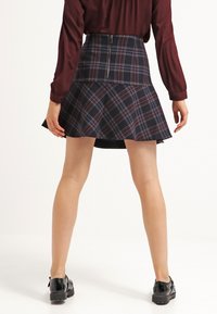 Navy rutmönstrad A-linjeformad kjol med en åtsittande midja och utställd nederdel, med en dragkedja bak. Bärs med en långärmad bordeauxblus och svarta skor.