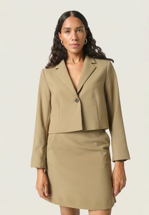 Cropped beige blazer with a single button closure, paired with a matching fitted skirt, smooth texture, and long sleeves.