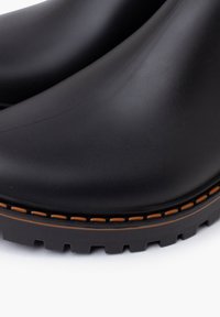 Bottines noires imperméables à la cheville avec une surface lisse, des coutures orange le long de la semelle et un fond texturé et robuste pour une meilleure adhérence.