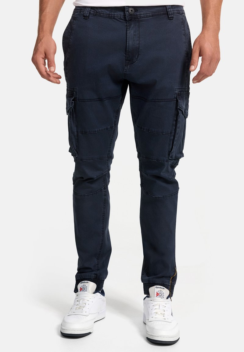 Navy cargo pants made of cotton blend, featuring multiple pockets, elastic cuffs, and stitching details. Worn with white sneakers.