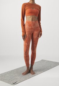 Orange ribbed long-sleeve top layered over a matching cropped sports bra, paired with high-waisted leggings featuring a faded pattern.