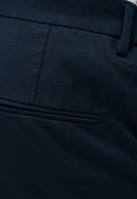 Tummansinisen laivastonsiniset housut, joissa on vyölenkit ja suljettu vaakasuuntainen takatasku hienovaraisilla ompeluista.