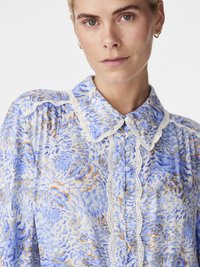 Blouse à motifs floraux bleus avec garniture en dentelle, col et fermeture à boutons. Caractérisée par un tissu doux et texturé avec des détails de design complexes.