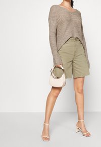 Ljusbrun stickad tröja med V-neck, olivgröna shorts med fransad nederkant, krämfärgad handväska och hudfärgade sandaletter med remmar.