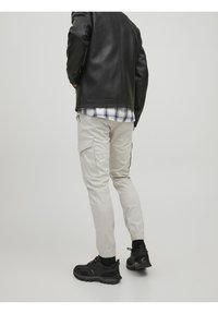 Vaaleanbeige cargo-housut, joissa on elastiset hihnat, sivutaskut ja hienoinen kiilto, yhdistettynä mustaan nahkatakkia ja mustiin lenkkarikenkiin.