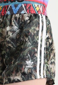 Schwarze Shorts mit einem tropischen Palmblattmuster, ausgestattet mit weißen Adidas-Streifen und Logo an der Seite. Elastischer Bund mit buntem Design.