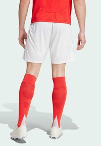Röd idrottströja med meshpanel, vita shorts och knälånga röda strumpor med texturerade mönster; bärs med vita fotbollsskor.