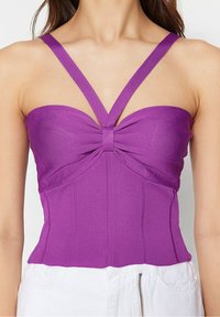 Haut sans manches violet avec un détail en nœud au centre, présentant des larges bretelles et un design ajusté en tissu texturé.